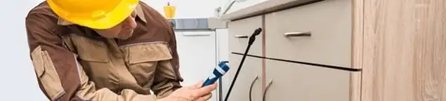 Roach exterminator applying treatment under kitchen cabinets in Fort Worth, TX