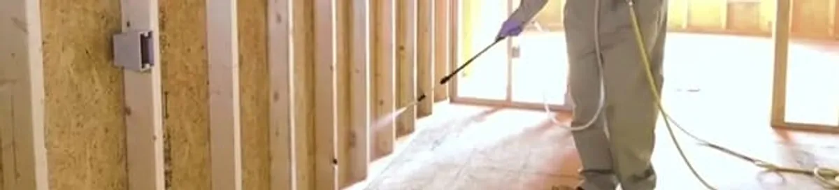 Termite treatment technician applying spray along framing and unfinished walls in Fort Worth, TX