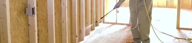 Termite treatment technician applying spray along framing and unfinished walls in Fort Worth, TX